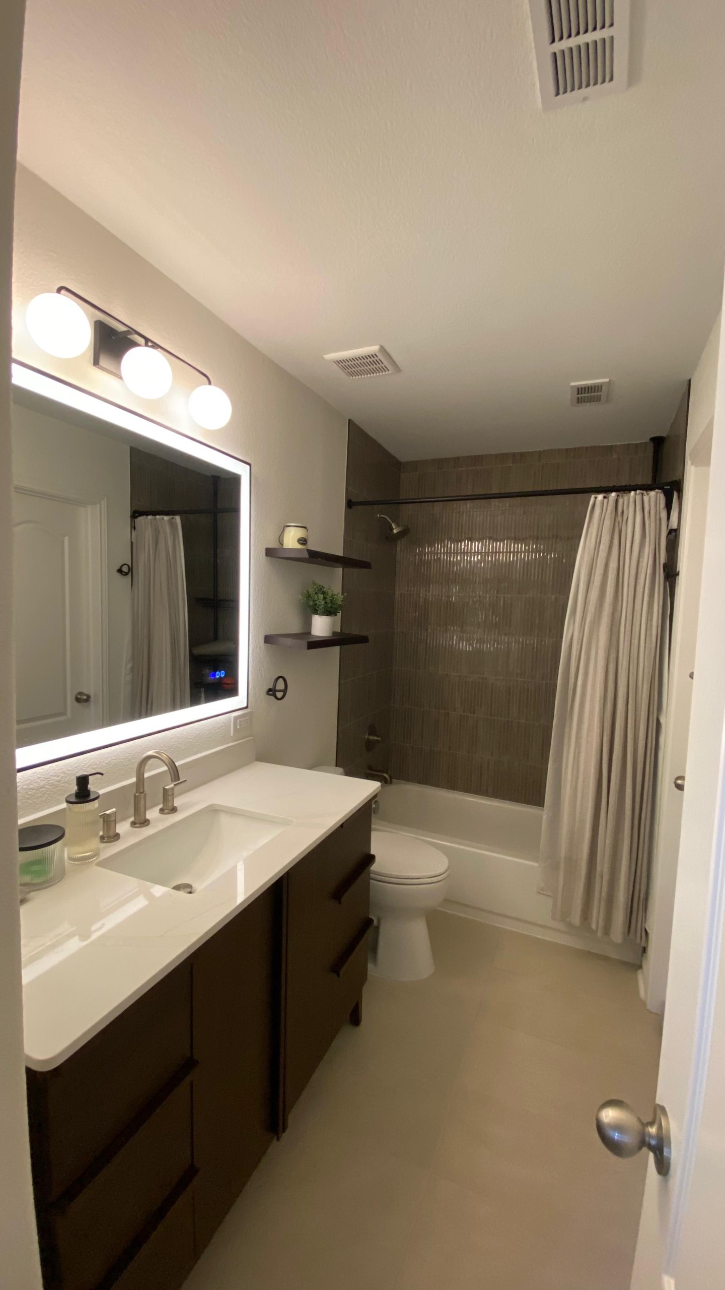 Modern bathroom renovation with brown tile shower, LED vanity mirror, and dark wood cabinetry